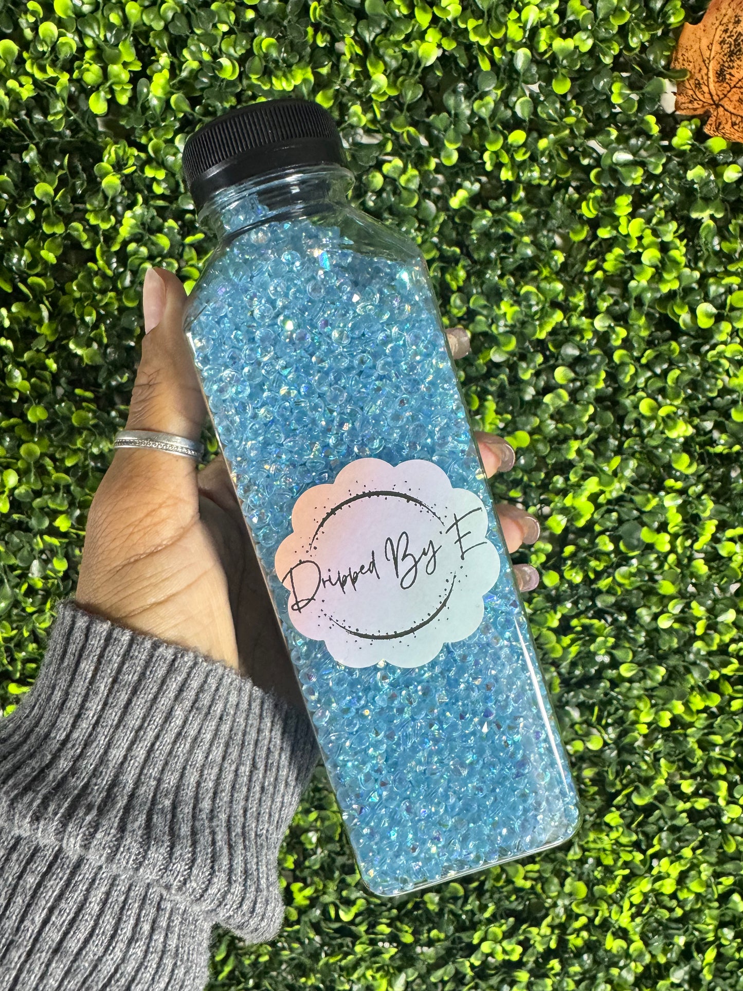 Hand holding a glittery water bottle with a brand logo against a grass background