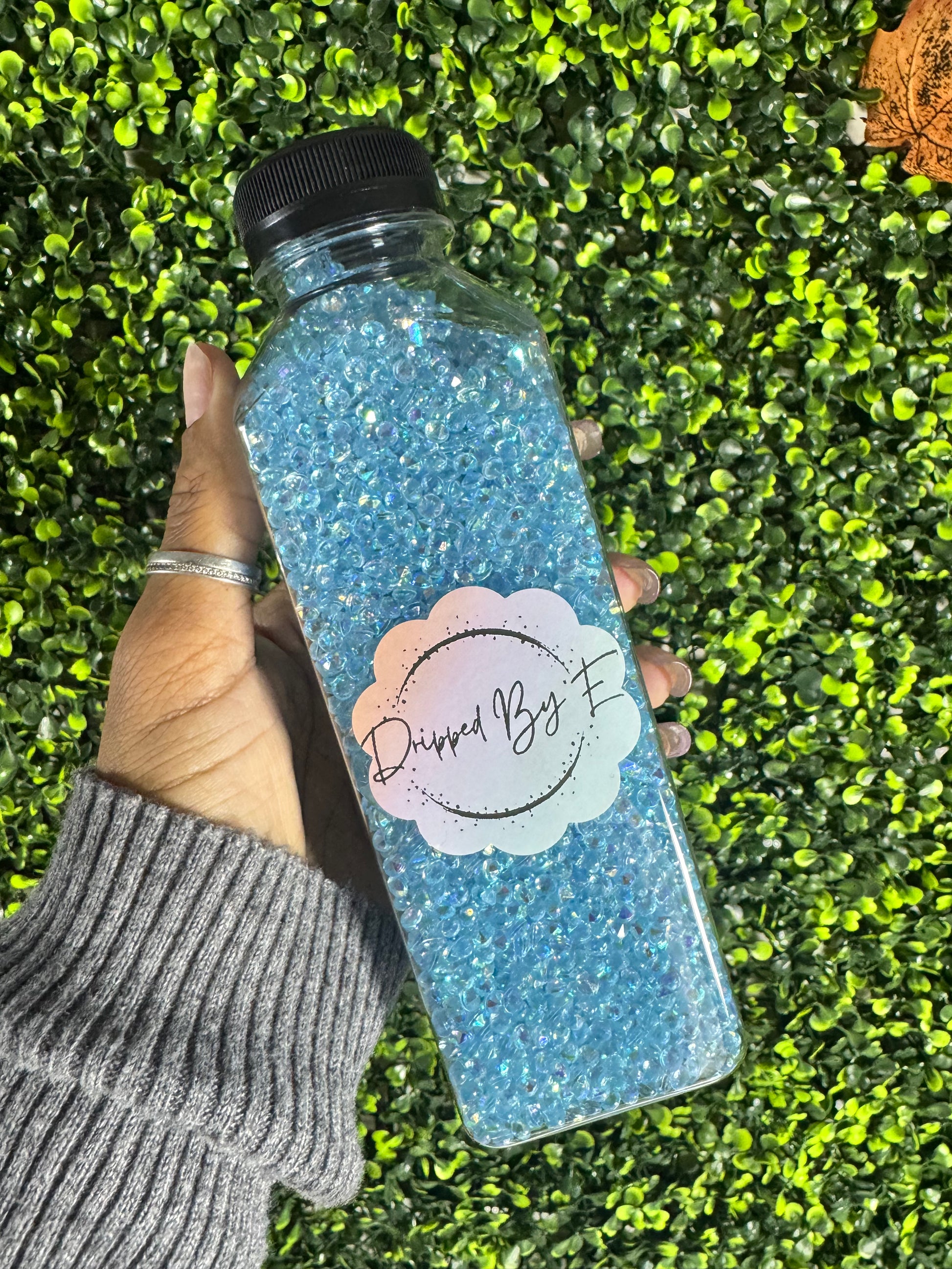 Hand holding a glittery water bottle with a brand logo against a grass background